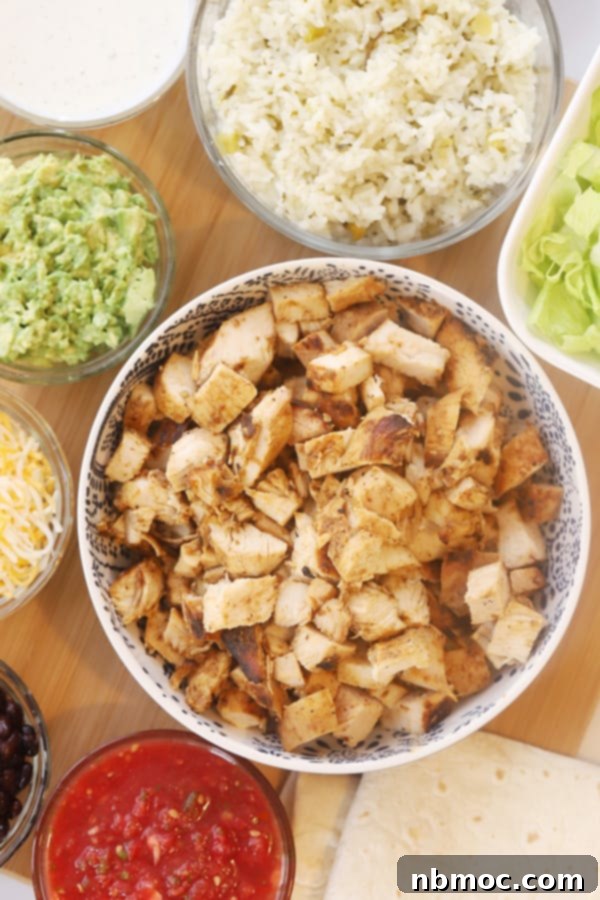 Restaurant-Style Chipotle Chicken Recipe 2 A bowl of delicious Copycat Chipotle Chicken served with side bowls of cheese, fresh guacamole, and other toppings, ready for creating burritos or bowls.