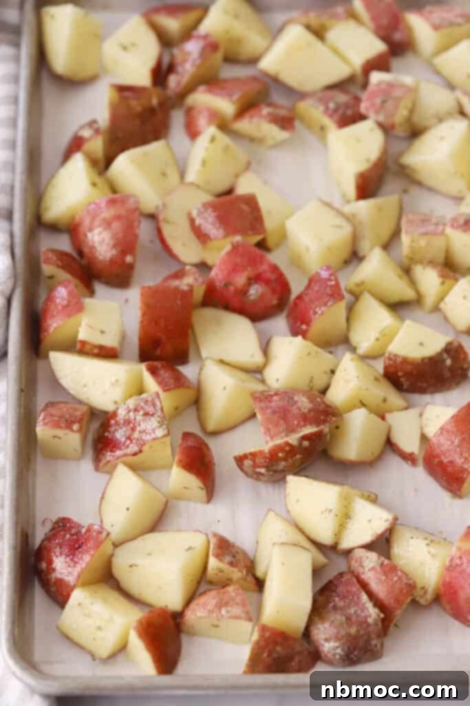 Quartered red potatoes on a sheet tray covered in parchment paper, neatly arranged before being roasted.