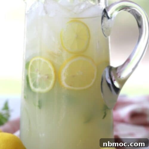 Mint lemonade in a clear pitcher with mint leaves and sliced lemons