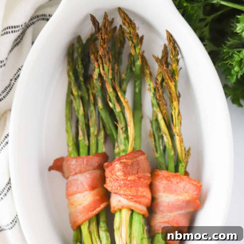 Crispy bacon-wrapped roasted asparagus spears, arranged on a baking sheet, illustrating a delicious holiday side dish recipe and a fantastic new Thanksgiving side.