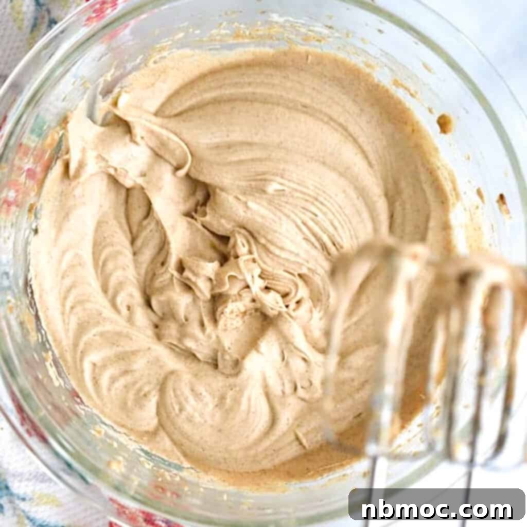 Homemade whipped cinnamon honey butter in a bowl, with an electric hand mixer nearby, ready to be spread. A perfect homemade honey butter for any bread.