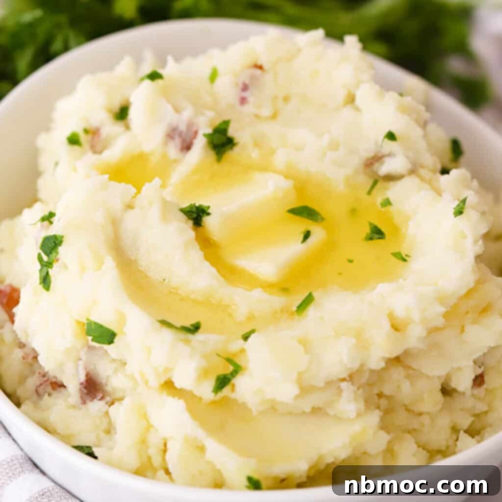 A large white bowl filled with rustic mashed red potatoes, garnished and ready to be served, highlighting their inviting texture.