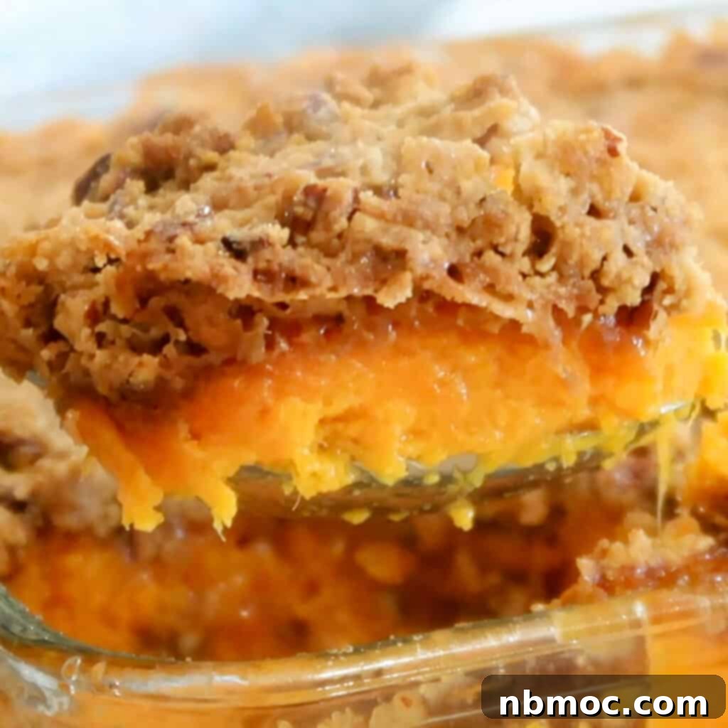 A close-up of a sweet potato casserole featuring a luscious pecan crumble topping, showcasing the crunchy texture over the smooth sweet potato base. The ideal pecan topping for sweet potato casserole.