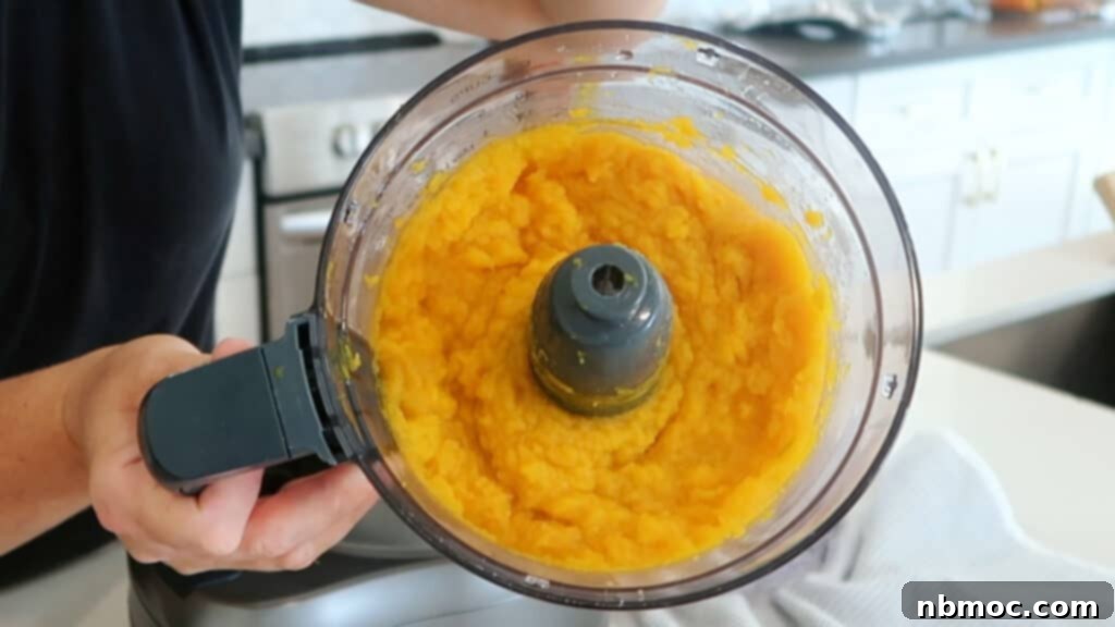 A food processor full of homemade fresh pumpkin puree, showcasing its smooth texture and vibrant color.