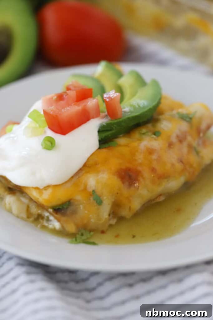 Ultimate Green Chile Chicken Enchiladas 7 A white plate with green chicken enchiladas topped with sour cream and avocados.