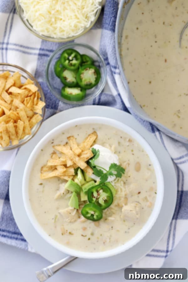 A bowl of creamy white chicken chili, elegantly garnished with golden tortilla strips, vibrant sliced jalapeños, and a generous sprinkle of shredded cheese, ready to be enjoyed.