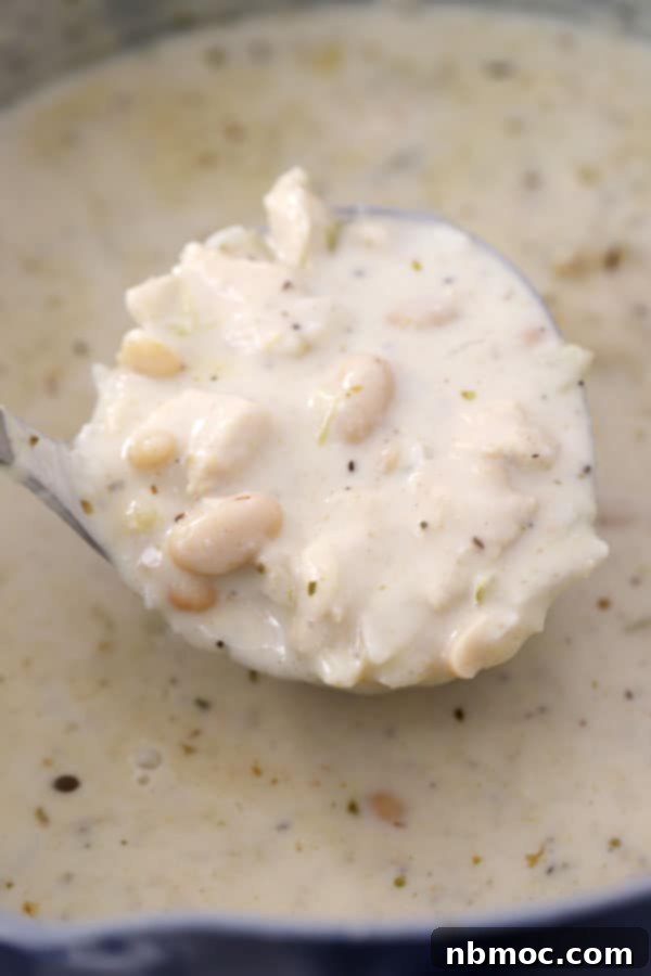 A large pot filled with creamy white chicken chili, adorned with a ladle, showcasing the rich texture and hearty ingredients within.