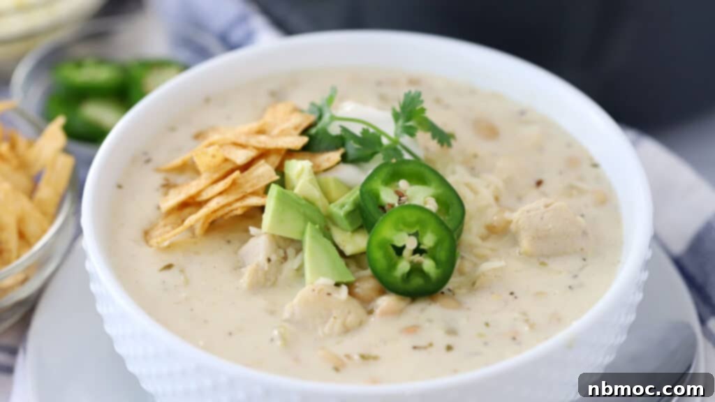 A small bowl of creamy white chicken chili, generously topped with vibrant shredded cheddar cheese, fresh jalapeño slices, and creamy avocado, ready to be savored.