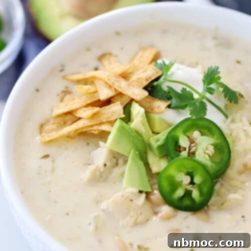 White chicken chili in a bowl, garnished with crunchy tortilla strips, creamy avocado slices, and vibrant sliced jalapenos, a perfect blend of texture and flavor.