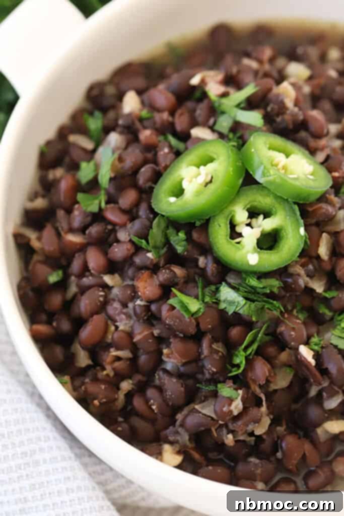 Smoky Chipotle Black Beans 2 A large bowl filled with homemade Chipotle black beans, garnished with vibrant sliced jalapeños and fresh cilantro, ready to be served.