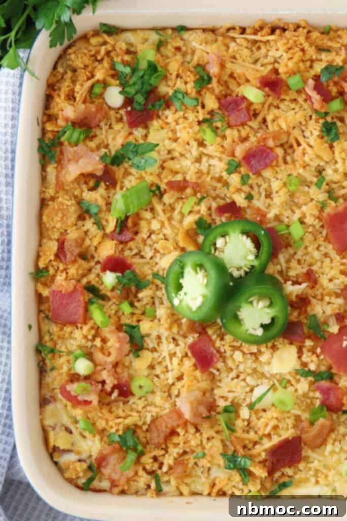 A baking dish filled with jalapeno popper dip, generously topped with crispy bacon bits and vibrant fresh sliced jalapenos, ready to be served as a party appetizer.