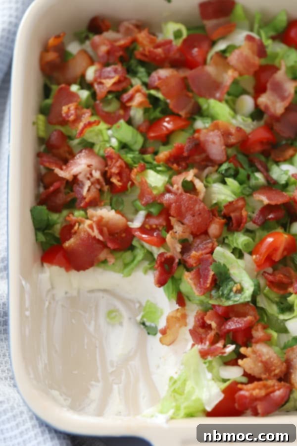 A baking dish with BLT Dip topped with bacon, lettuce, and tomato, ready to be served.