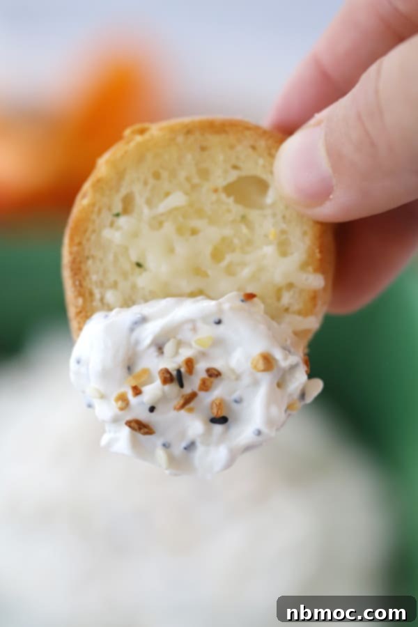 A hand holding a sliced baguette dipped in Everything Bagel Dip.