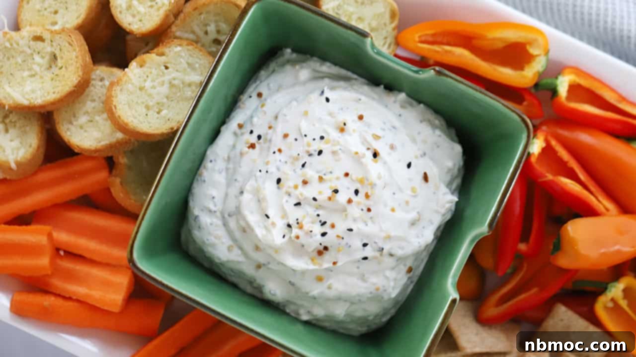 A serving bowl full of Everything Bagel Dip surrounded by fresh veggies and crostini.