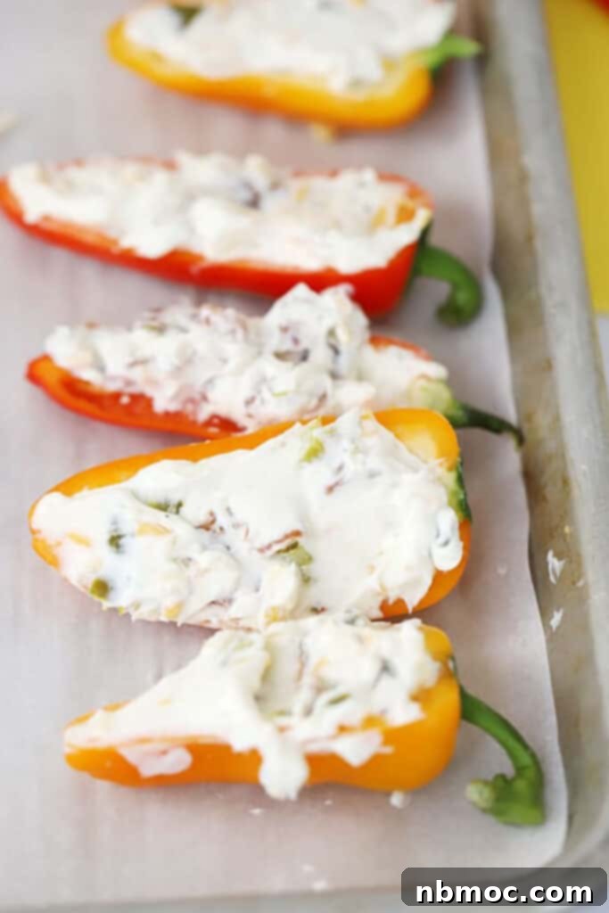 A baking sheet filled with colorful mini bell peppers stuffed with a creamy cheese mixture, ready for baking. The peppers are neatly arranged, showcasing their vibrant red, yellow, and orange hues.