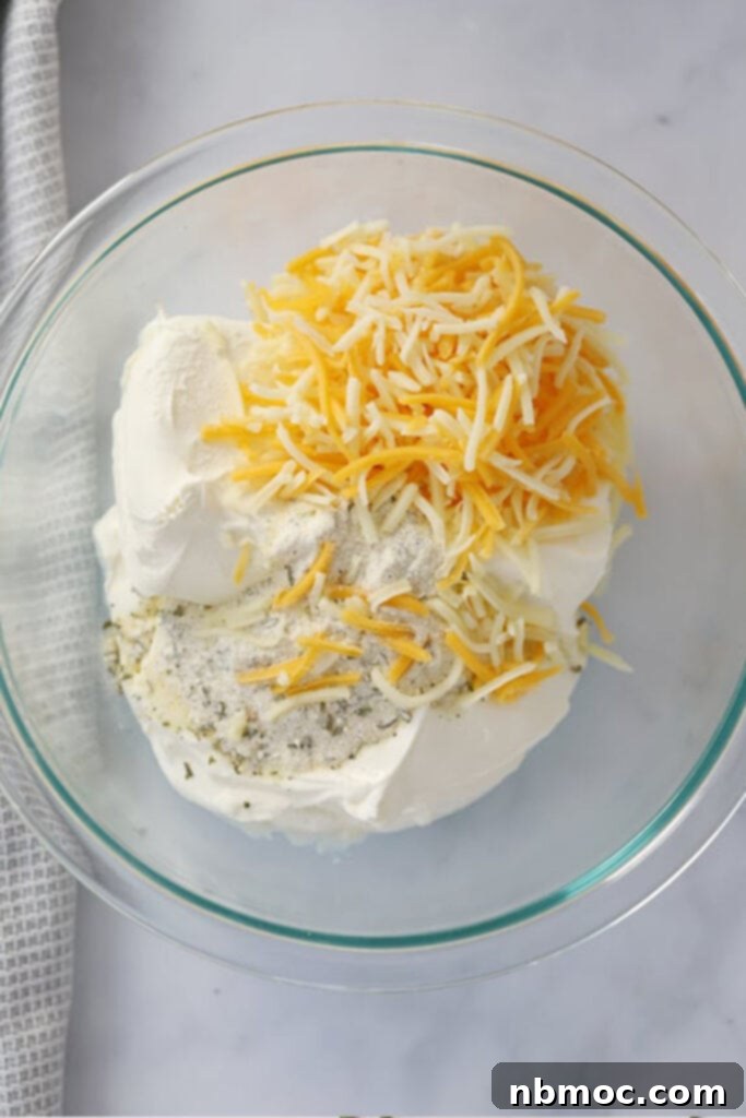 A glass mixing bowl holds a creamy, white mixture, the perfect ranch-flavored cream cheese filling for stuffed bell peppers. A spatula rests in the bowl, indicating readiness for stuffing.