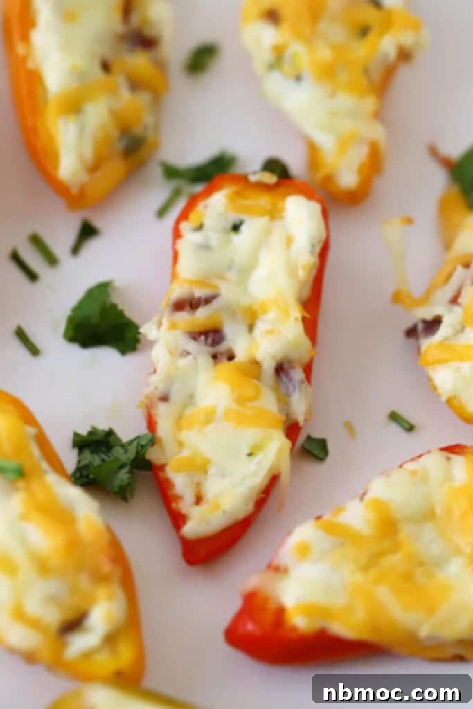 A close-up of baked cream cheese stuffed peppers on a serving platter, garnished with fresh herbs. The cheese is perfectly melted and golden, highlighting the deliciousness of this easy appetizer.