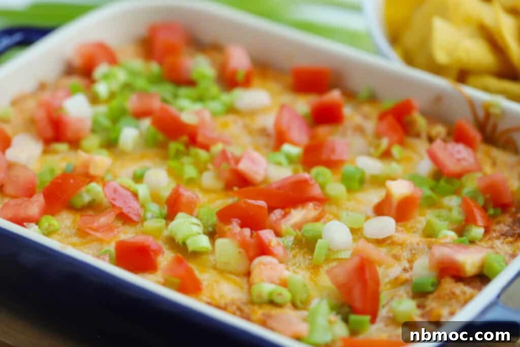 Cream cheese bean dip served hot with tortilla chips, showcasing its melted cheese and vibrant toppings.
