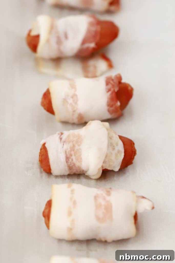 Crispy Bacon Wrapped Smokies 3 Lil smokies wrapped in bacon on a baking sheet ready to cook.
