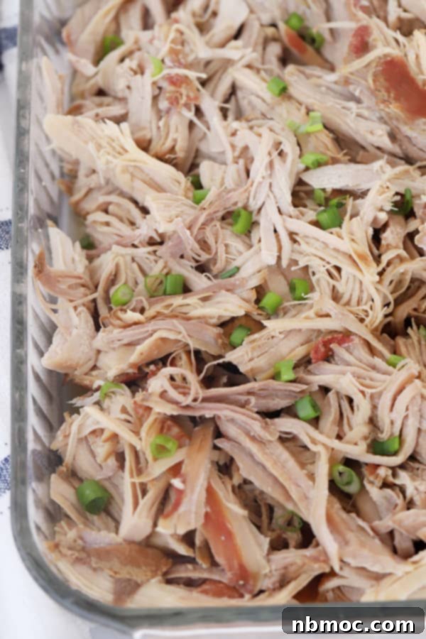 Shredded Kalua Pork in a baking dish topped with chopped scallions.