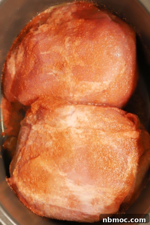 Pork roast in a slow cooker with seasoning on top, ready to be cooked.