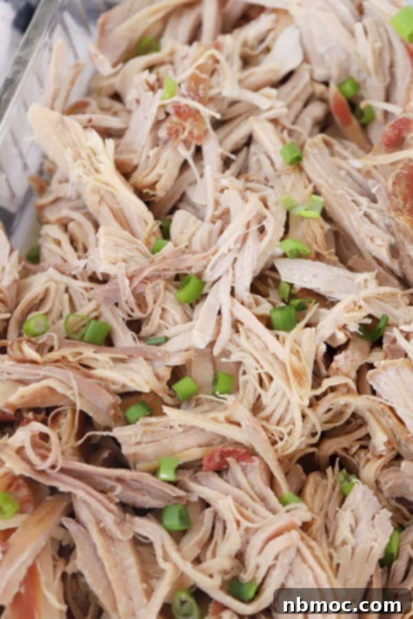 Kalua pork in a baking pan topped with chopped scallions, ready to be served.