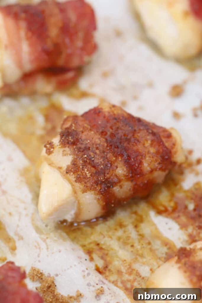 Bacon-wrapped chicken bites arranged neatly on a parchment-lined baking sheet, ready for the oven.