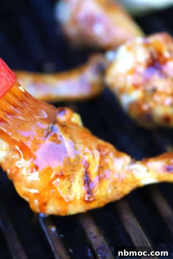 Chicken drumsticks on a grill with a brush adding buffalo sauce.
