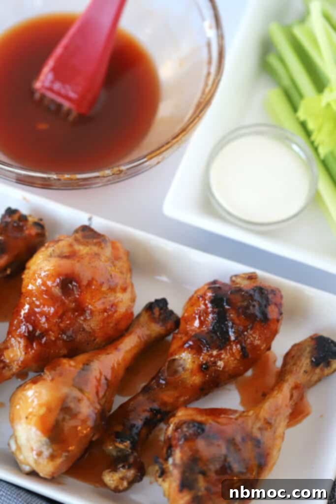 A platter with buffalo drumsticks next to a bowl with buffalo sauce and another plate with celery.