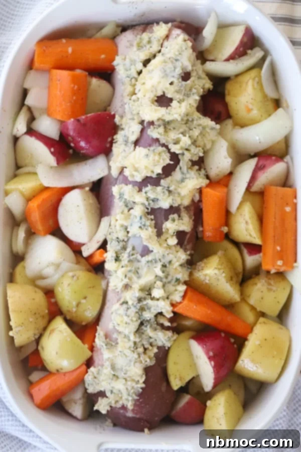 Garlic Herb Pork Tenderloin with Roasted Potatoes 2 pork tenderloin and potatoes and carrots covered in herb butter and vegetables in a baking dish.
