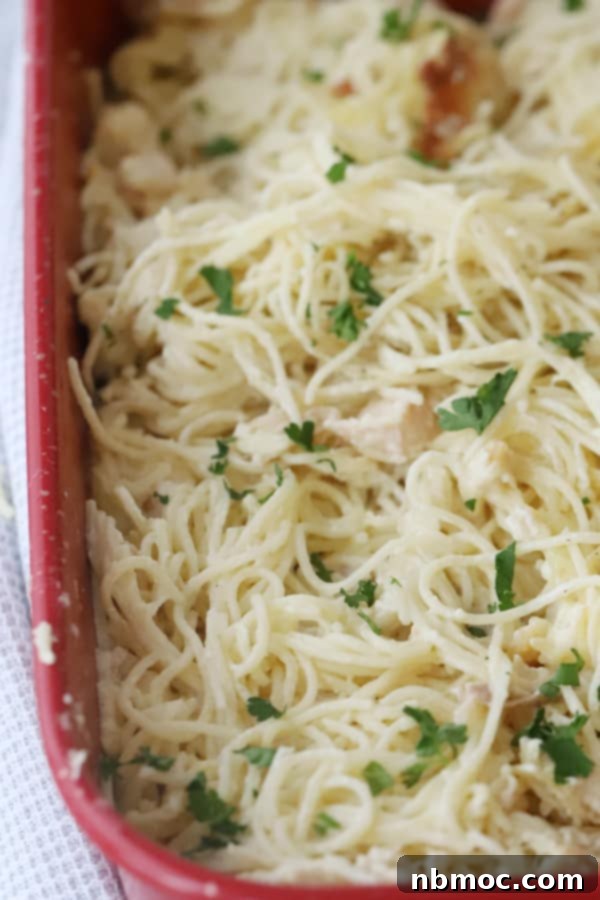 Baked Chicken and Spaghetti with cream cheese in a red baking dish, topped with fresh parsley.