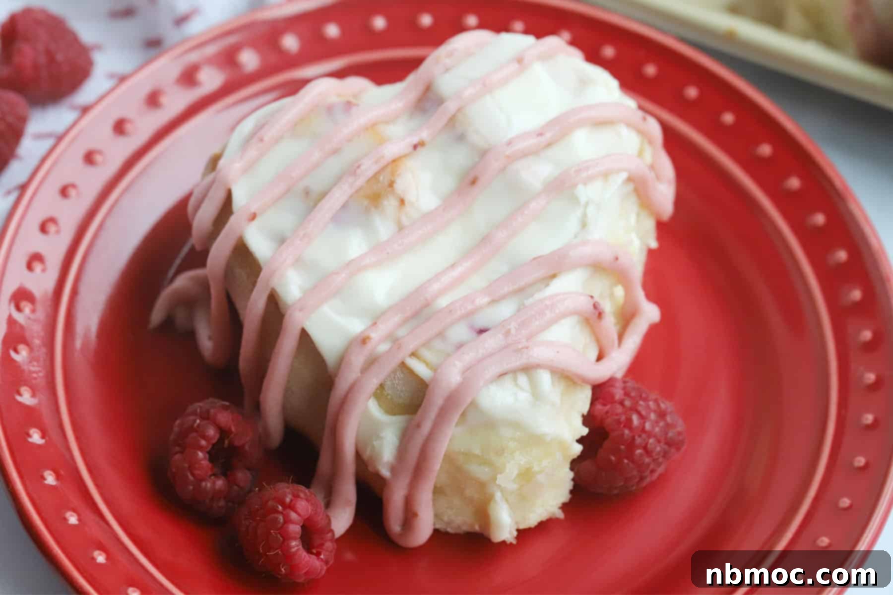 Baked raspberry sweet roll with lemon cream cheese frosting, decorated with raspberry drizzle, served for Valentine's Day.