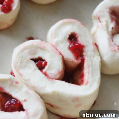Closeup of an unbaked raspberry sweet roll, showing the vibrant filling and spiraled dough, ready for baking.