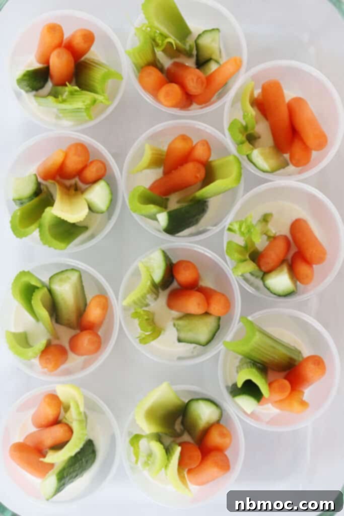 A plate full of individual appetizers in a cup, made with ranch dressing on the bottom and fresh carrots, celery, cucumbers.