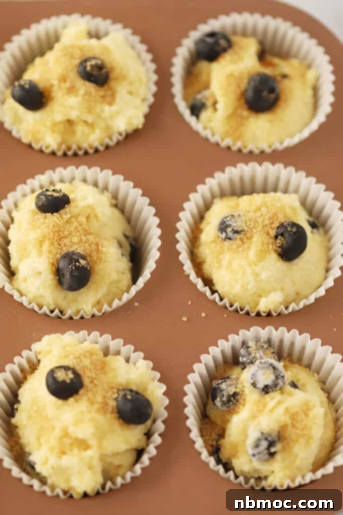 Sunshine Berry Muffins 3 Lemon blueberry muffin batter in a cupcake pan with liners, some topped with a shimmering sugar crust