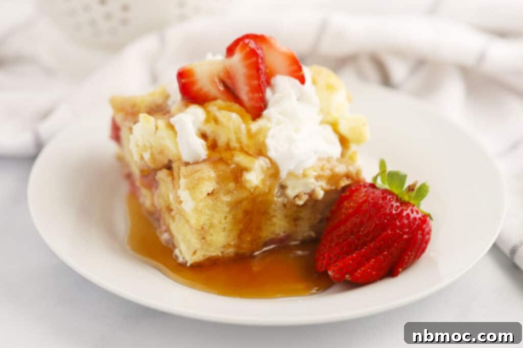 Baked strawberry cream cheese French toast on a plate, topped with fresh whipped cream and strawberries, ready to be served.