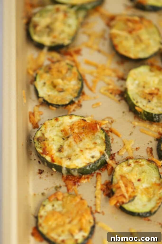 A baking sheet full of perfectly roasted zucchini slices topped with golden-brown Parmesan cheese, fresh out of the oven.