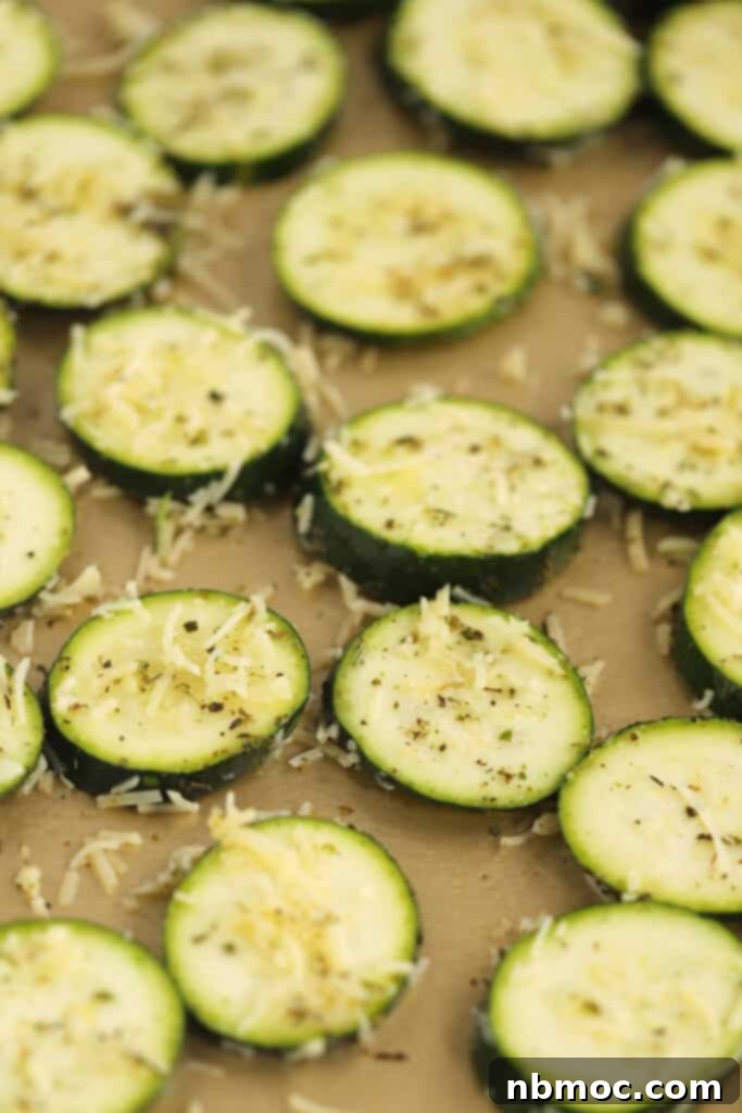 Fresh, uncooked zucchini slices, seasoned and arranged in a single layer on a baking sheet, ready to be baked.