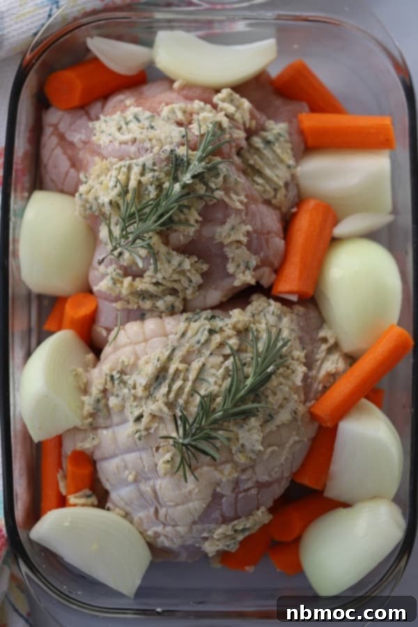 Raw turkey breast covered with herbed butter, ready to bake in the oven with carrots and onions in a baking dish. 