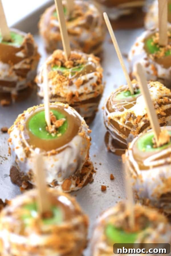 A large baking sheet showcasing homemade caramel apples drizzled in white chocolate and topped with crushed candy.