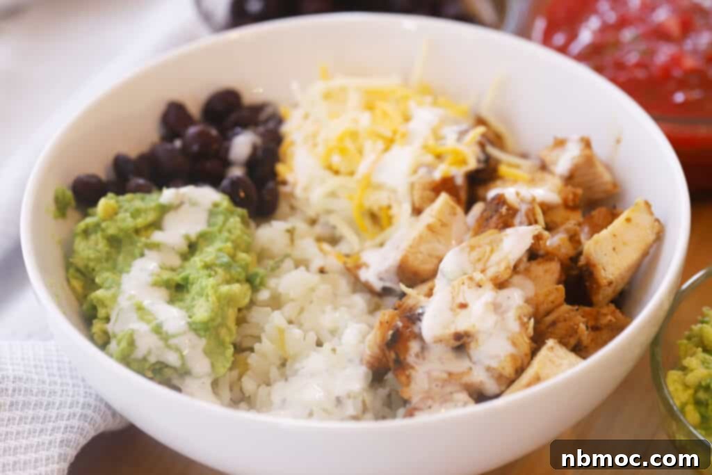 A vibrant white bowl generously filled with fluffy rice, tender chipotle chicken, seasoned black beans, rich guacamole, and shredded cheddar cheese, ready to be enjoyed.