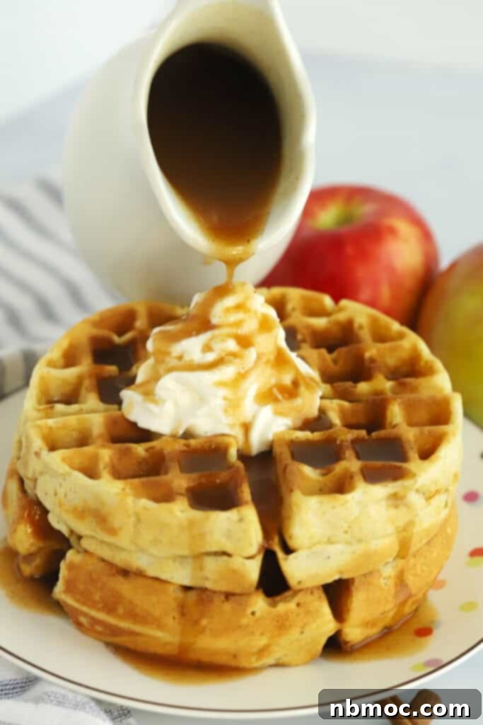A small pitcher pouring apple syrup over waffles and whipped cream.