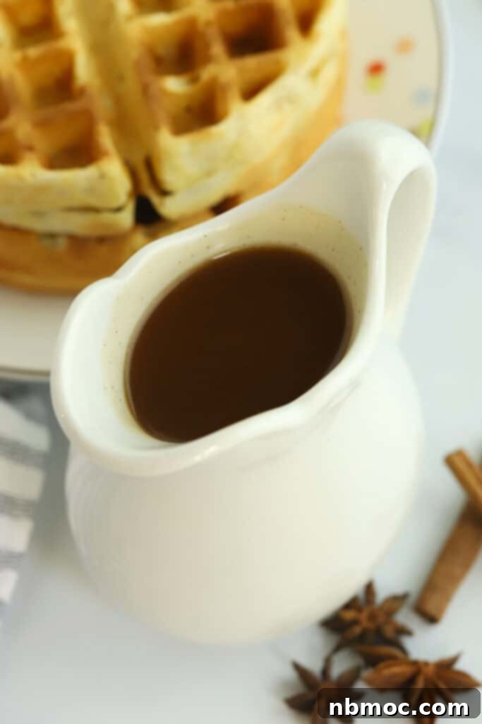 Apple cider syrup in a small white pitcher with waffles in the background.