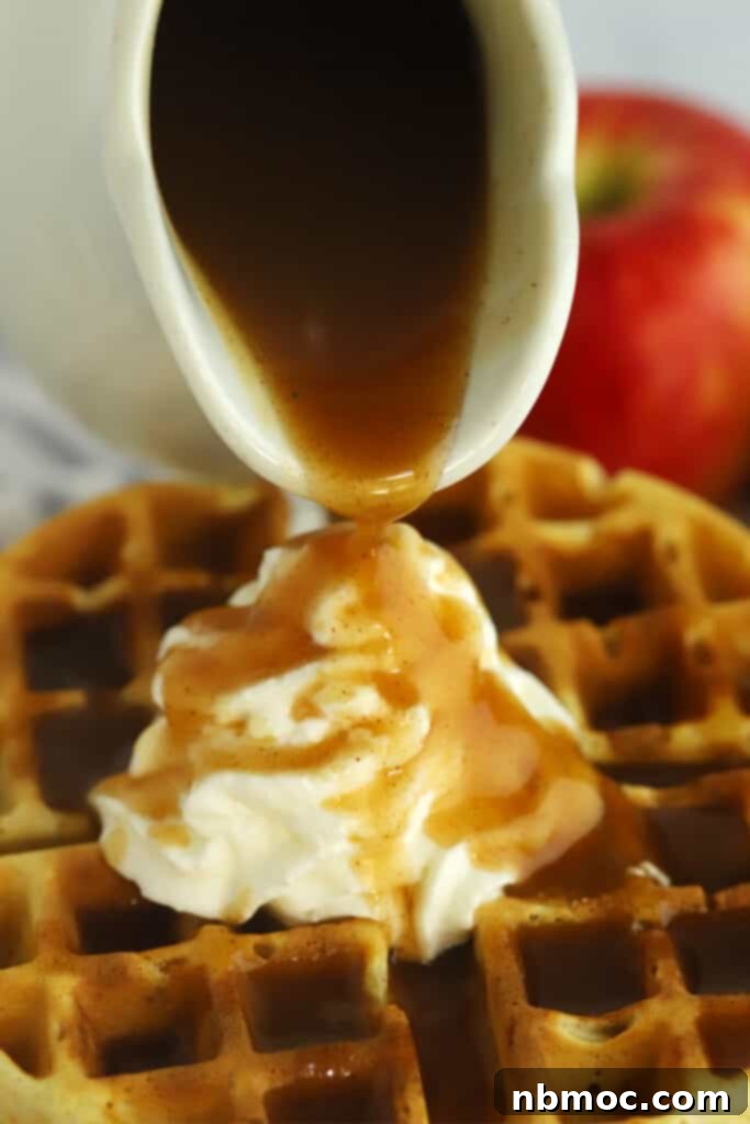 Apple brown sugar syrup poured from a carafe over waffles and whipped cream.
