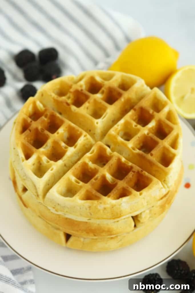 A stack of golden brown homemade Belgian waffles on a white plate, ready to be topped.