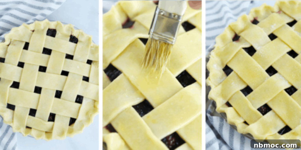 A hand brushing an egg wash over the lattice top of a blackberry pie before baking.