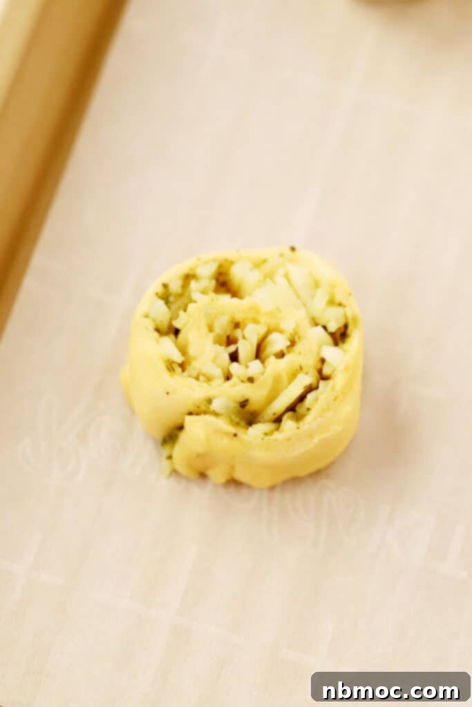 Savory Pesto Swirls 4 A rolled-up crescent roll dough, filled with pesto and cheese, sliced into individual pinwheels on a baking sheet, ready for the oven. This highlights easy appetizers with crescent rolls.