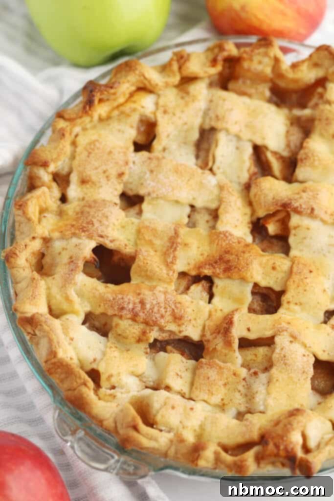 A fresh baked homemade apple pie with a lattice pie crust in a glass pie plate on a table. 