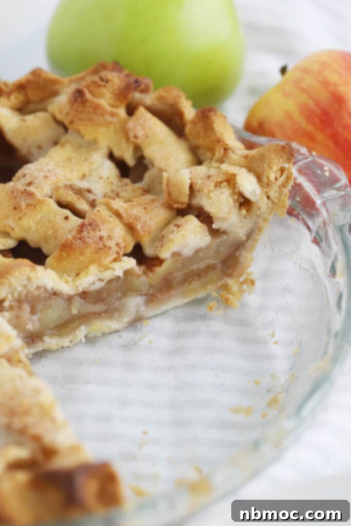 A glass pie plate with an apple pie that has a slice removed.