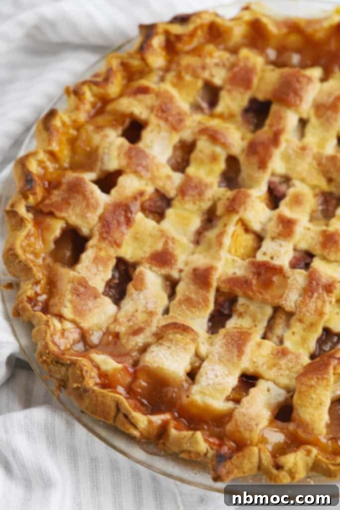 Sun-Kissed Peach Pie 2 A full peach pie baked inside a pie plate with a lattice top crust.